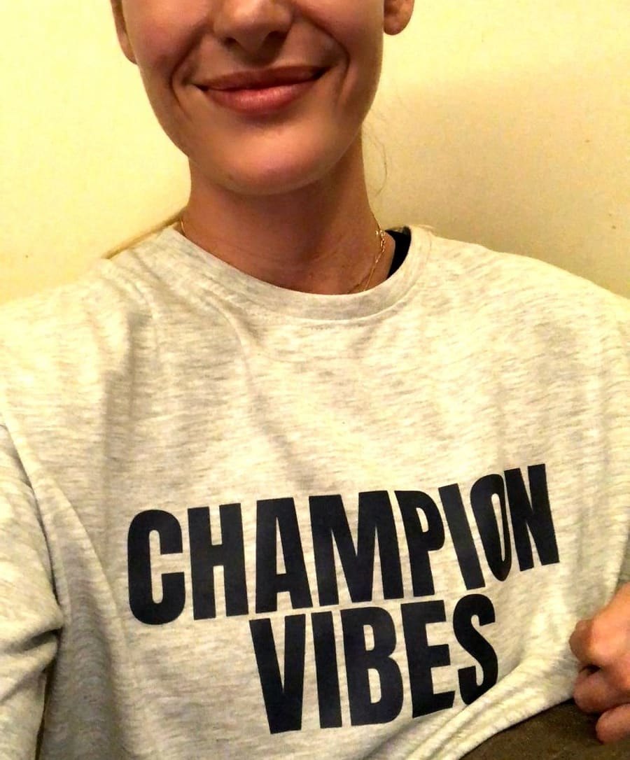 Close-up of a grey CHAMPION VIBES sweatshirt worn by a smiling wearer