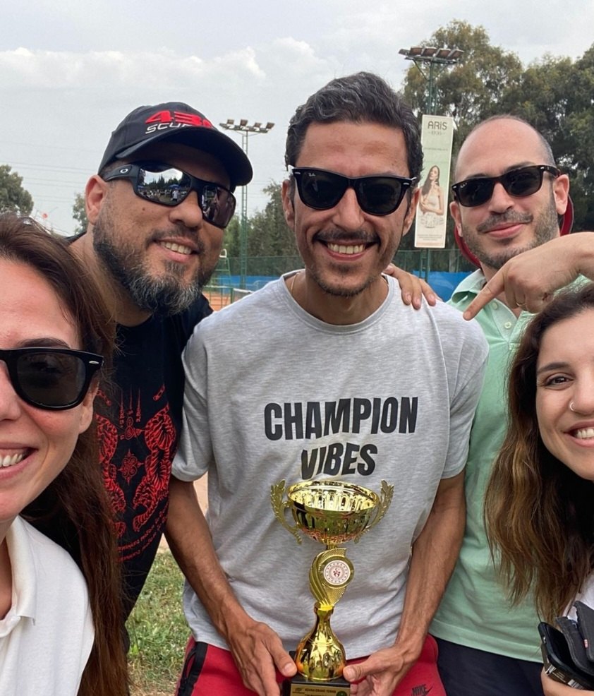 A group of friends around a trophy winner wearing a grey CHAMPION VIBES tee